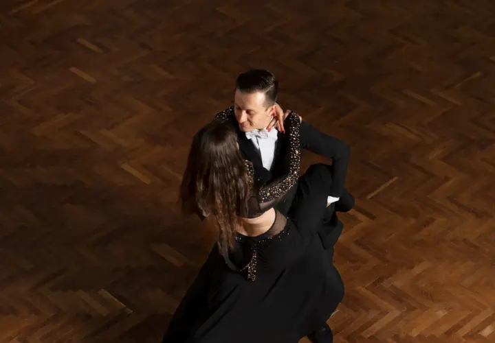 Para tańczy tango argentyńskie, wykonując skomplikowane kroki na drewnianym parkiecie.