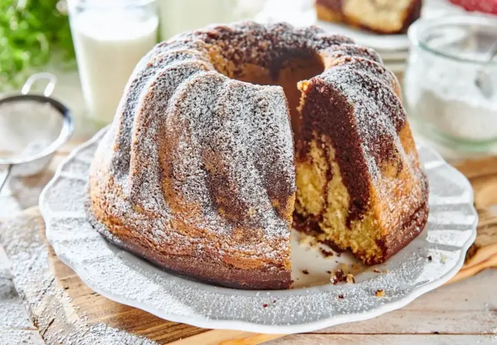 Puszysta babka na oleju z polewą z cukru pudru, z kawałkiem odciętym, by pokazać jej marmurkowe wnętrze.