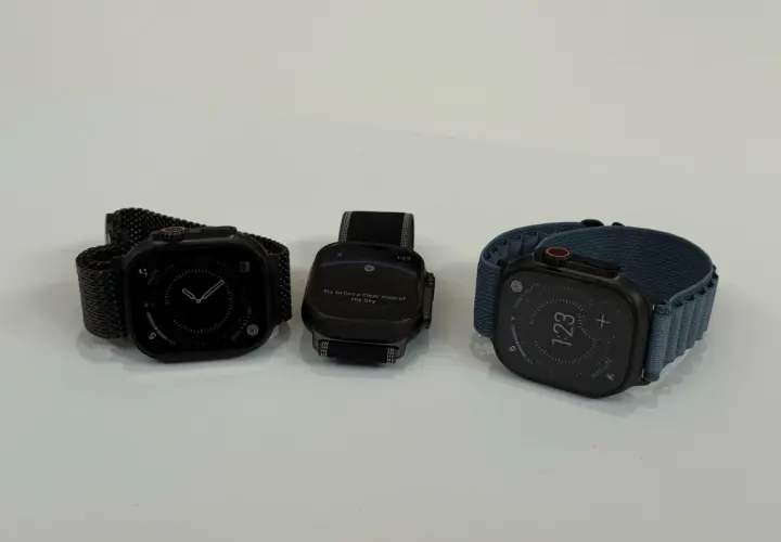 Trzy zegarki Apple Watch na białym tle: jeden z czarną bransoletą, drugi z czarną, trzeci z niebieską.