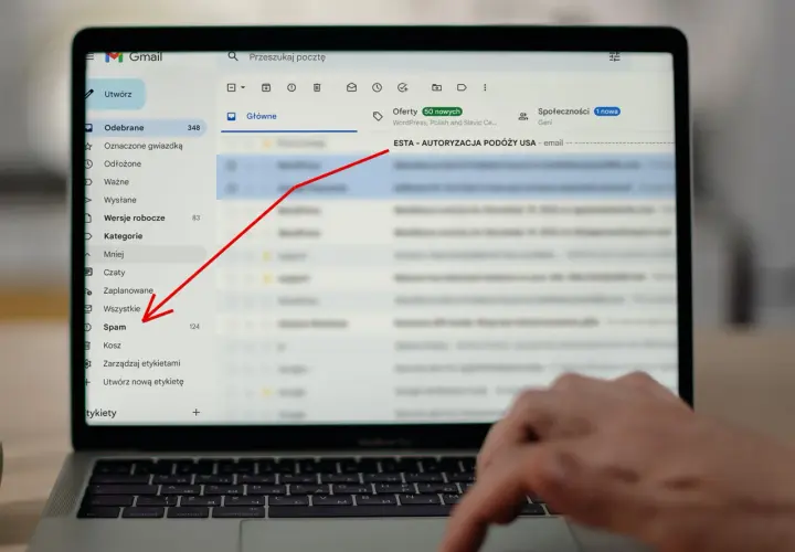 Laptop z otwartym mailem Gmail, zaznaczony folder "Spam" i czerwona strzałka wskazująca na temat maila "ESTA - AUTORYZACJA PODÓŻY USA".