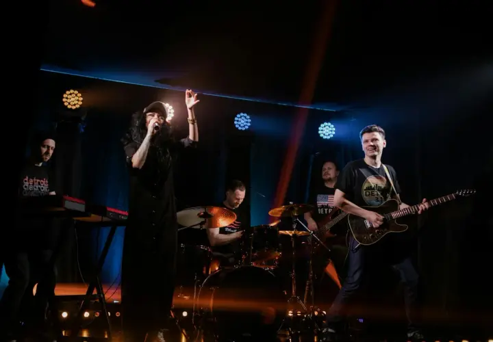 Energiczny zz trio rockowe na scenie. Wokalistka w czarnej sukience, gitarzysta, basista, perkusista i klawiszowiec tworzą dynamiczny zespół.