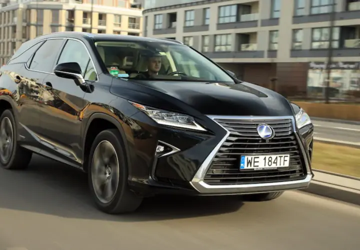 Czarny Lexus RX 450h jedzie ulicą w mieście, za nim widać nowoczesne budynki.