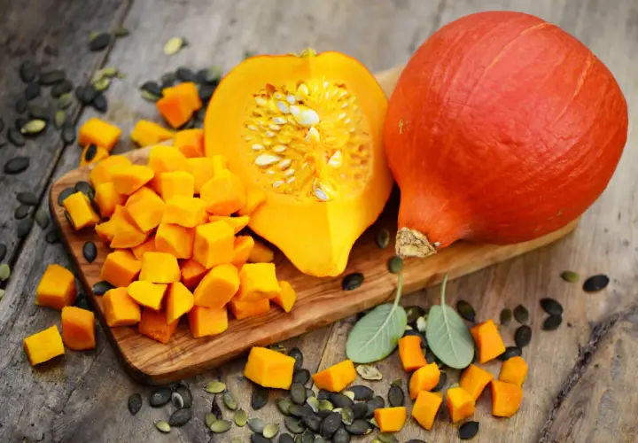 Pomarańczowa dynia hokkaido, pokrojona w kostkę i w całości, z pestkami i listkami szałwii. Idealna do uprawy i pysznych potraw.