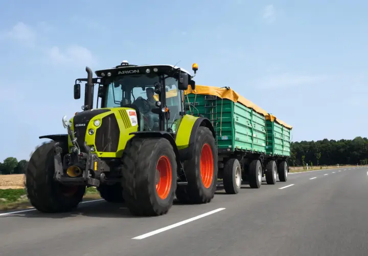 Ein Claas Arion Traktor mit Anhängern fährt auf der Straße. Der Fahrer hat die Fahrerlaubnis L und transportiert landwirtschaftliche Güter.
