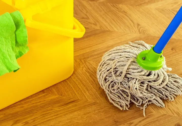 Cubo amarillo con paño verde y una mopa o fregona lista para limpiar el suelo de madera.