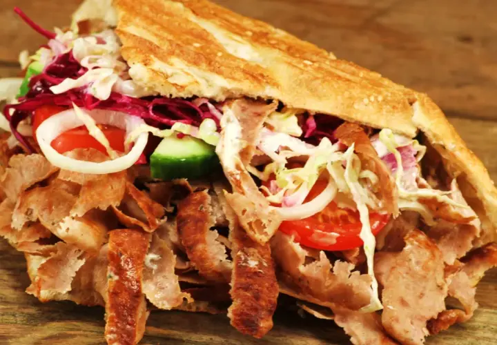 Kebab z mięsem, warzywami i sosem w bułce na drewnianym tle.