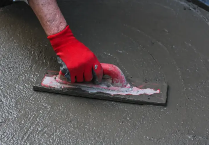 Ręka w czerwonej rękawicy wygładza świeży beton. To kluczowy etap prac, który wpływa na to, jaka grubość posadzki w garażu będzie optymalna.