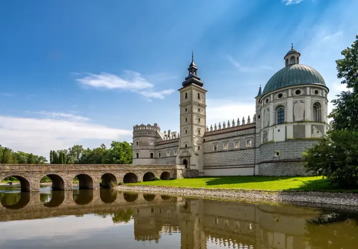 Zamek w Krasiczynie, majestatyczna budowla z wieżą i kopułą, odbija się w spokojnej tafli wody.