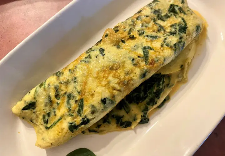 Une omelette aux épinards, dorée et moelleuse, servie sur une assiette blanche. Un délice simple et sain.