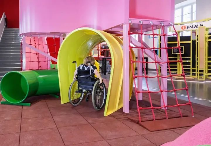 En person i rullstol navigerar genom en färgglad lekplats på Teknikmuseet Stockholm.