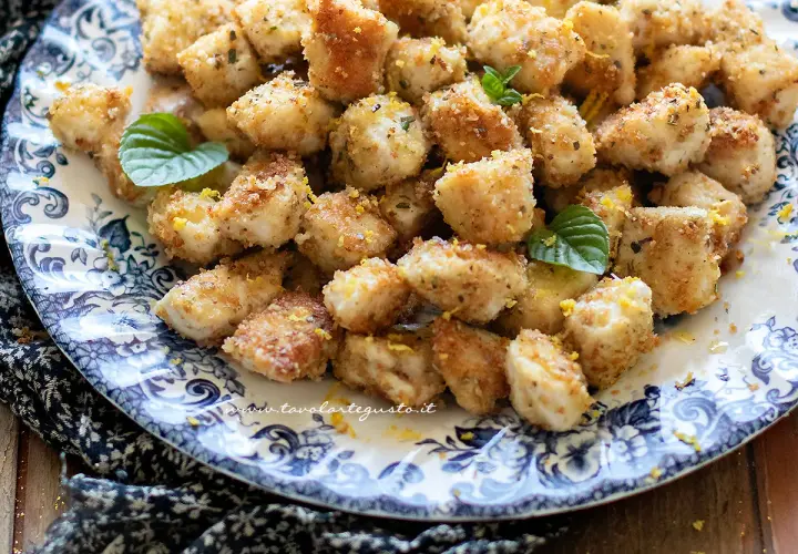 Bocconcini di pollo dorati e croccanti, guarniti con scorza di limone e foglie di menta fresca, serviti su un piatto decorato.