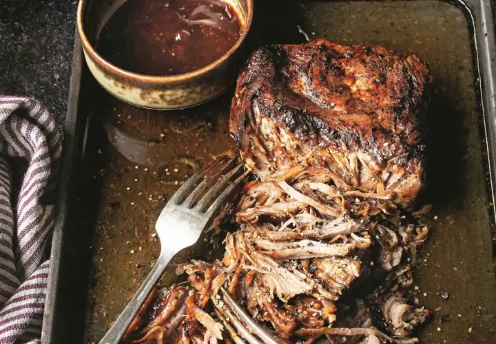 Soczysta, szarpana wieprzowina z sosem barbecue na blasze. Widoczne widelce ułatwiające rozrywanie mięsa.