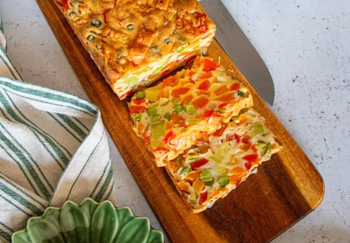 Tranches colorées d'une terrine de légumes savoureuse, garnie de poivrons, carottes et petits pois, prête à être dégustée.