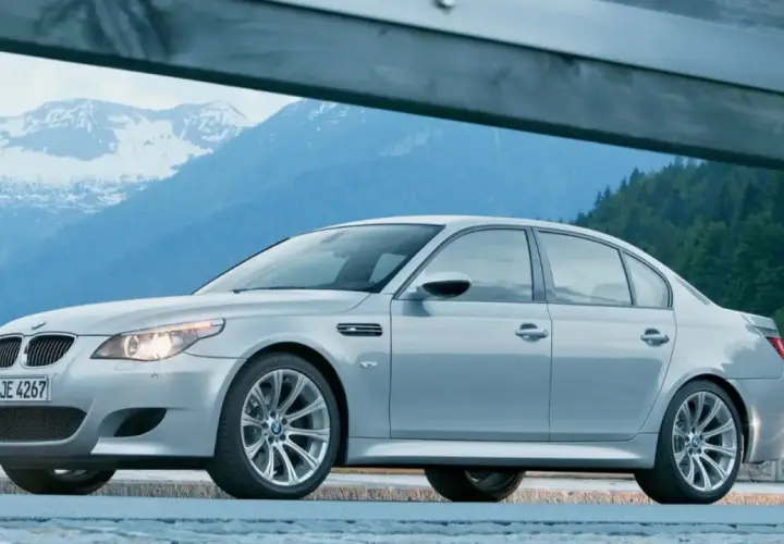 Un elegante BMW M5 E60 plateado descansa ante un paisaje montañoso nevado, listo para la aventura.