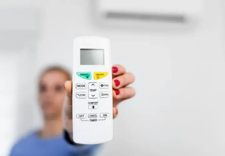 Mano sostiene control remoto de aire acondicionado, listo para activar el símbolo del frío y disfrutar de un ambiente fresco.