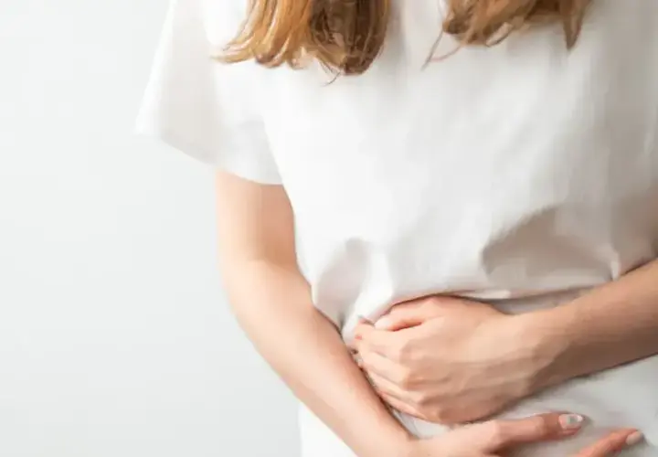 Donna con le mani sull'addome, che esprime disagio e difficoltà a digerire.
