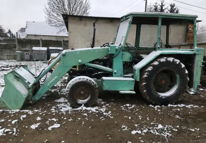 Zielona koparka Ostrówek stoi na błotnistym terenie, pokryta śniegiem.