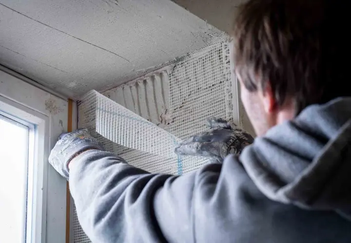 Hand mit Handschuh verputzt Fensterlaibung mit Armierungsgewebe.