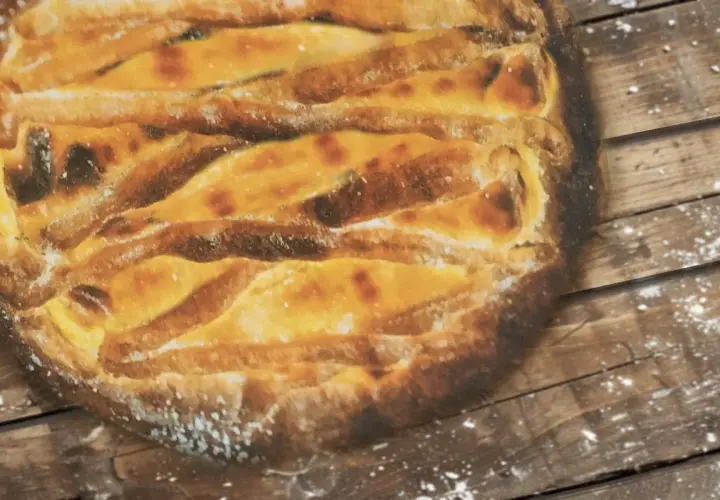 Une tarte au libouli dorée, aux croisillons de pâte bien cuits, repose sur un fond de bois rustique saupoudré de farine.