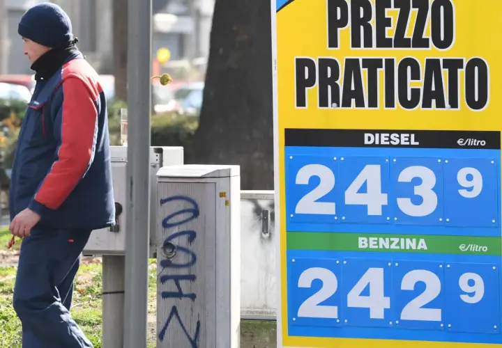 Prezzo praticato per la benzina: 2,429 €/litro. Un uomo in divisa osserva il cartello.