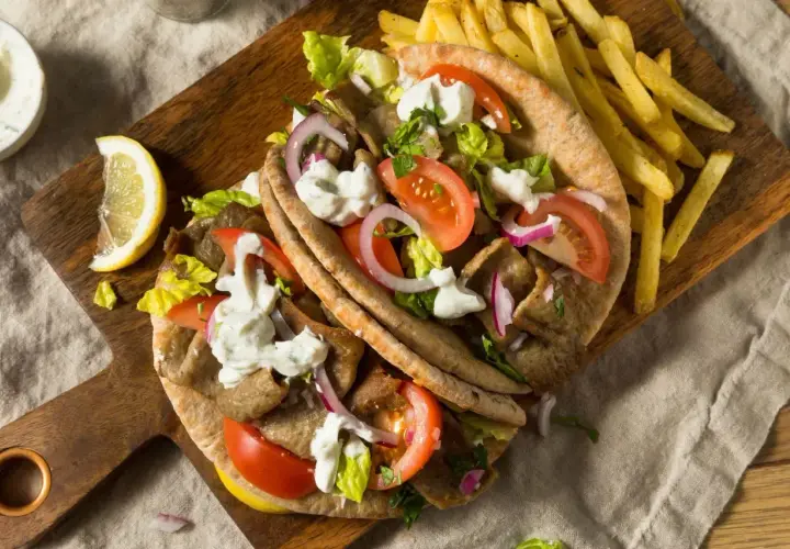 Pyszny grecki gyros z kawałków mięsa opiekanego na rożnie, podany z frytkami, warzywami i sosem.