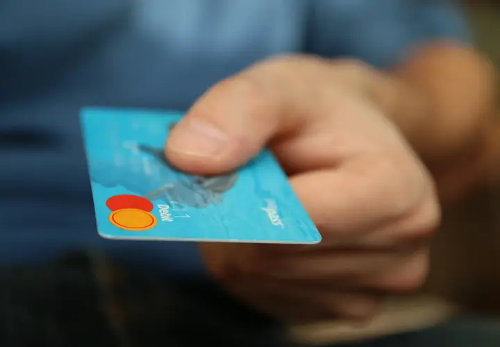Main d'une personne tenant une carte bancaire bleue. L'inconvénient d'une carte à autorisation systématique est qu'elle peut être refusée si le solde est insuffisant.