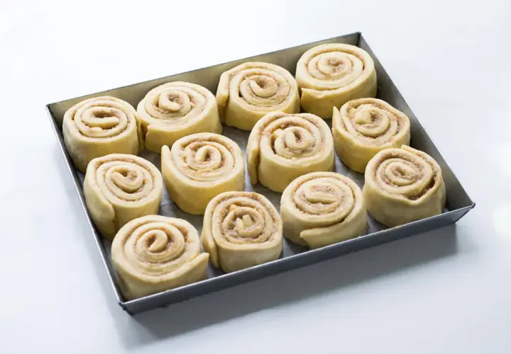 Rotolini alla cannella e mela pronti per essere infornati, disposti in una teglia.