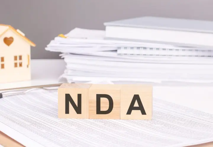Cubos de madera con las letras NDA, una casa de juguete y pilas de documentos.