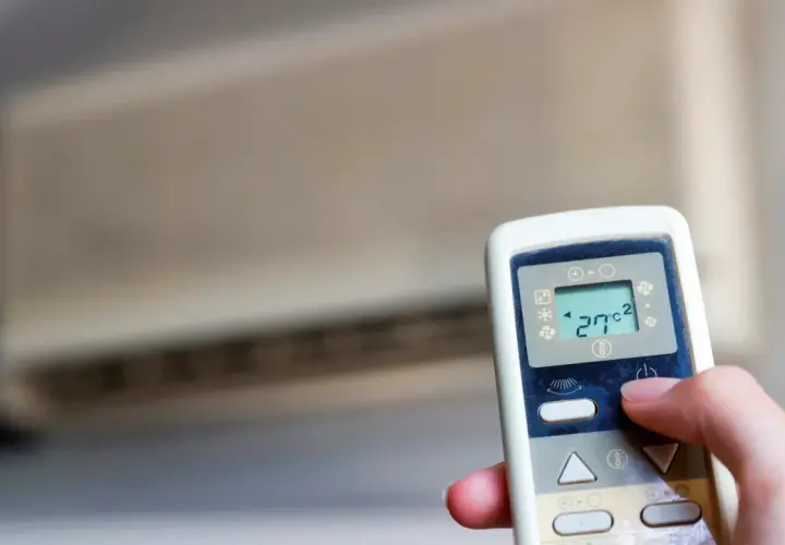 Mano ajustando el control remoto de un aire acondicionado cool o heat. La pantalla muestra 27°C.