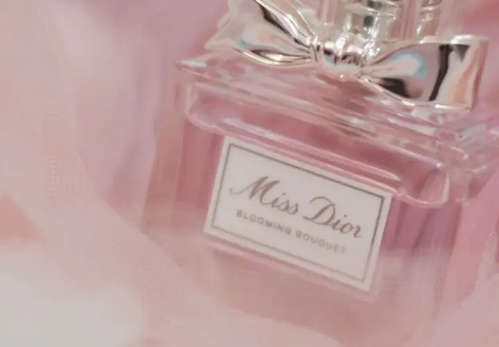 Frasco de perfume Miss Dior Blooming Bouquet, con un lazo plateado, sobre tela rosa suave. Un toque de elegancia para la madame de rosa.