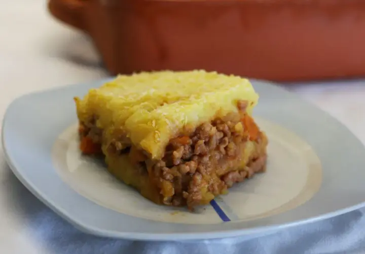 Un trozo de pastel de carne tradicional con puré de patatas gratinado, servido en un plato azul claro.