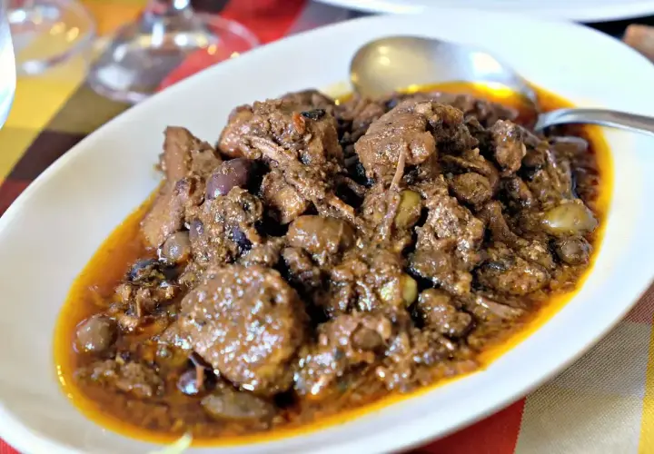 Un saporito cinghiale alla cacciatora, con olive e una ricca salsa, servito in un piatto bianco.
