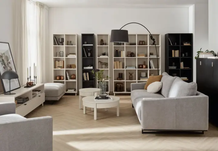 Nowoczesny living room z szarą sofą, regałami pełnymi książek i dekoracji, okrągłym stolikiem kawowym i lampą łukową.