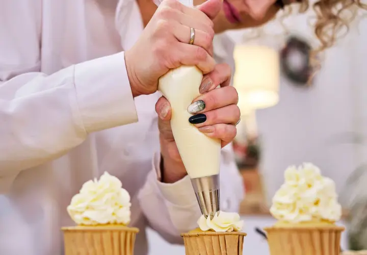 Pâtissière décorant des cupcakes avec une poche à douille. La crème est d'une belle couleur ivoire, parfaite pour savoir quel colorant pour chantilly mascarpone utiliser.