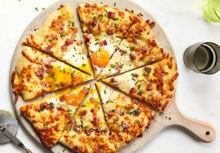 Kawałki pizzy carbonara z jajkiem sadzonym, boczkiem i szczypiorkiem, pokrojone na desce.