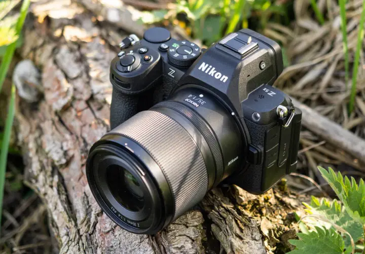 Aparat Nikon Z5 II z obiektywem Nikkor 35mm f/1.4 leży na spróchniałym drewnie, otoczony zielenią.