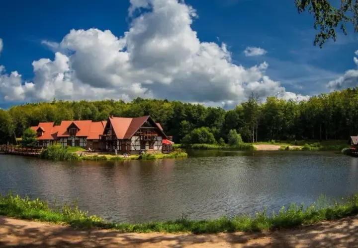 Idealne miejsce na długi weekend w sierpniu: urokliwe domki nad jeziorem, otoczone lasem, z pięknym niebem i chmurami.