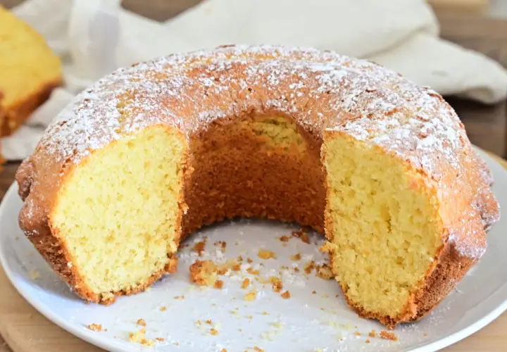Una ciambella soffice, cosparsa di zucchero a velo, attende di essere gustata. La sua consistenza invitante promette un momento di puro piacere.