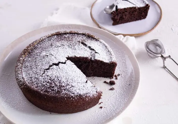 Gâteau au chocolat saupoudré de sucre glace, une part coupée. Idéal pour savoir par quoi remplacer le beurre dans un gâteau au chocolat.