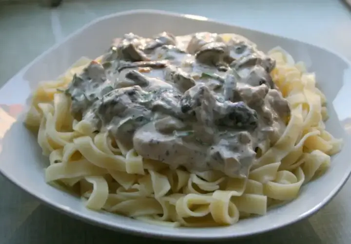 Pyszne tagliatelle z grzybami w kremowym sosie, podane na białym talerzu. Idealne danie dla miłośników grzybów.