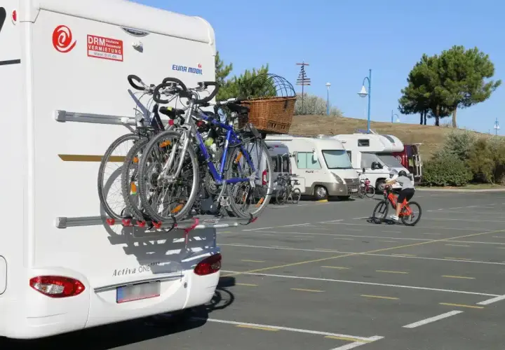 Camping-car avec vélos à l'arrière. Un cycliste s'entraîne sur un parking. Avis sur aire de camping-car.