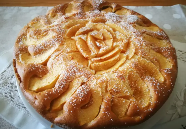 Una deliziosa torta di mele senza glutine, decorata con fettine di mela a forma di rosa e spolverata di zucchero a velo.