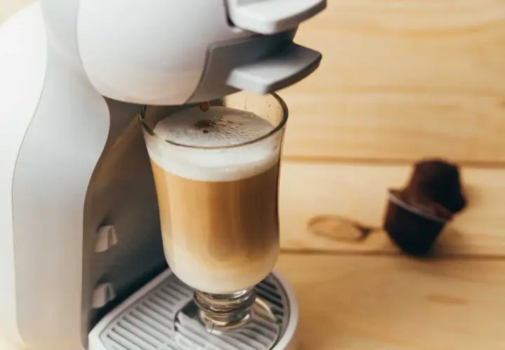 Kawa w kapsułkach: czy jest zdrowa? Ekspres przygotowuje latte, obok leży kapsułka.