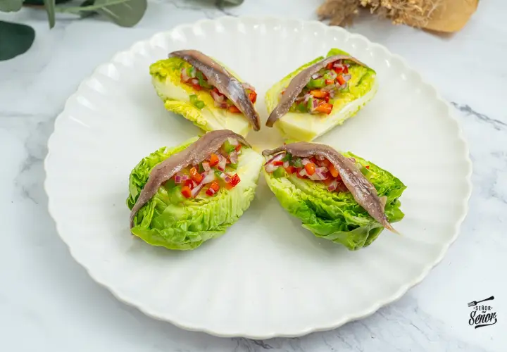 Cuatro cogollos de lechuga rellenos de pimientos y cebolla picados, coronados con anchoas. Un bocado fresco y sabroso.