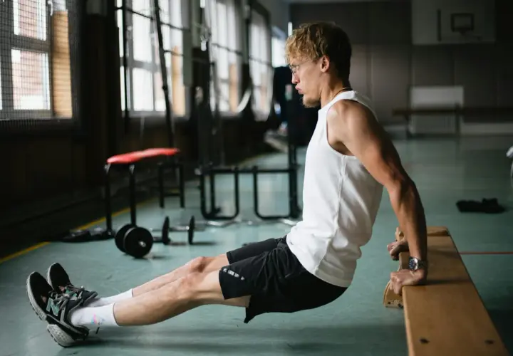 Mężczyzna wykonuje ćwiczenie dipy na triceps, opierając dłonie o ławkę.