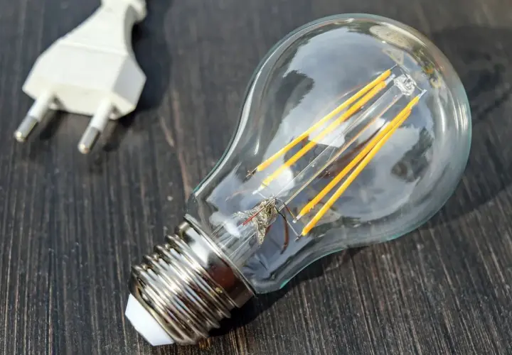 Żarówka LED i biała wtyczka na ciemnym drewnianym tle. Symbolizują potencjał, który czeka na aktywację, jak współczynnik jednoczesności w technologii.
