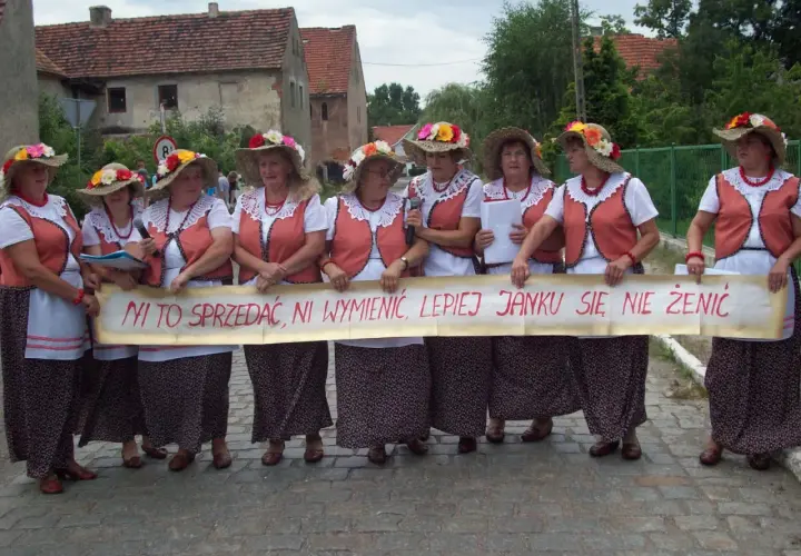 Kobiety w ludowych strojach trzymają transparent z napisem "Ni to sprzedać, ni wymienić, lepiej Janku się nie żenić" - śmieszne teksty na bramy weselne.