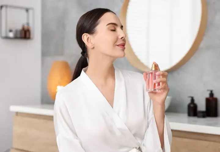 Kobieta w szlafroku rozpyla perfumy. Mgiełka od perfum różni się intensywnością zapachu i trwałością.