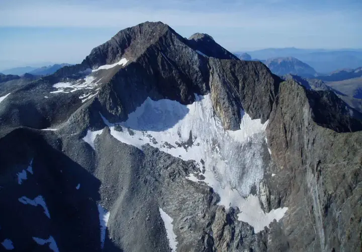 Majestuoso pico perdiguero cubierto de nieve y roca, con un glaciar que desciende por sus laderas.