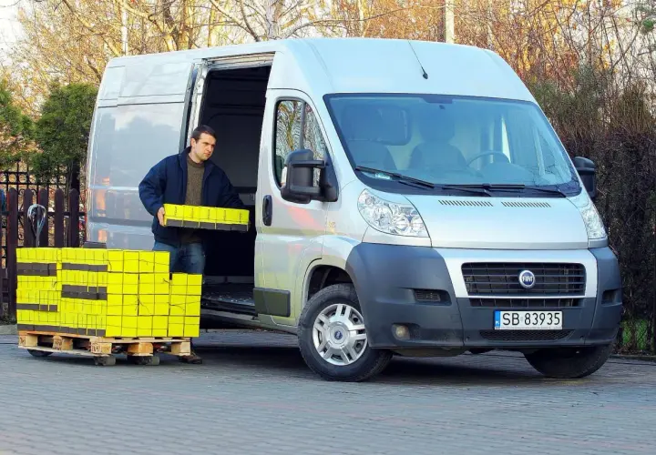 Mężczyzna rozładowuje żółte paczki z Fiata Ducato 2.3.